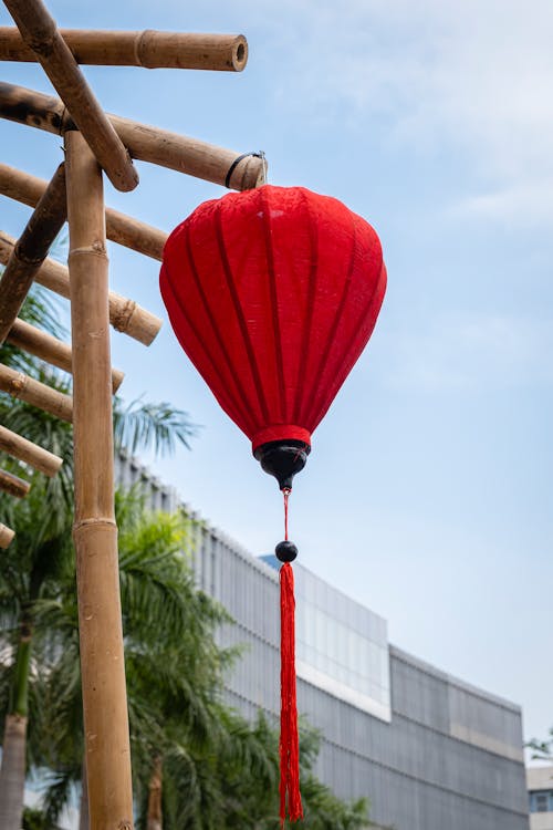 From below of bright red Chinese lantern hanging on bamboo railing in city street in sunny day