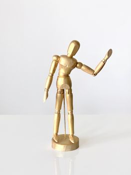Gold-painted wooden artist mannequin posing on a white surface in a bright studio.