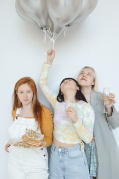 Three women celebrating with balloons, cake, and wineglasses indoors.