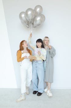 Three women celebrating a birthday indoors with balloons and cake.