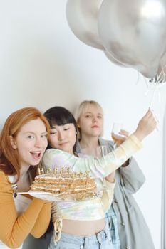 Three women celebrating with cake and balloons, capturing a joyful moment of togetherness.