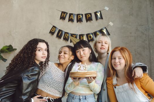 Five friends celebrate a 25th birthday with a cake and decorations indoors.