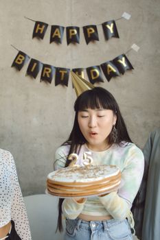 Young woman in party hat blowing birthday candles on cake indoors.