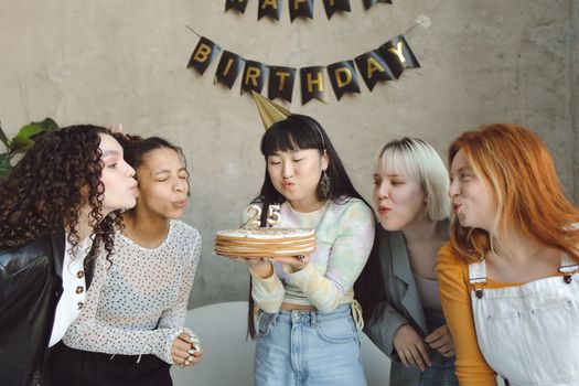 Group of diverse women celebrating a 25th birthday indoors with cake and decor.