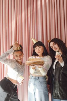 Group of young women celebrating a birthday with cake and party hats indoors.