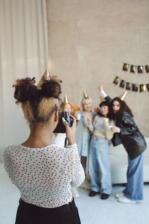 Free Joyful group of friends in party hats pose for a photo while a woman photographs them indoors. Stock Photo