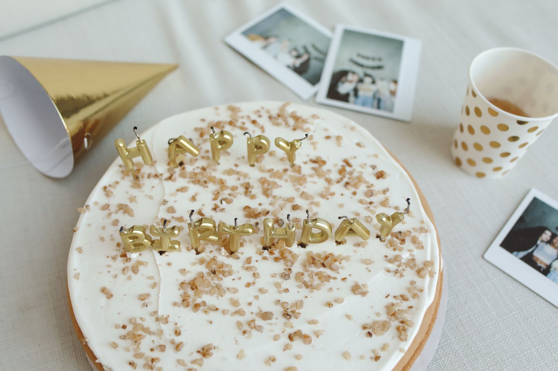 Top-down view of a birthday cake with gold lettering, surrounded by party decor and photos.