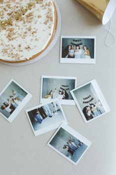 Top view of Polaroid photos surrounding a birthday cake on a light tablecloth.