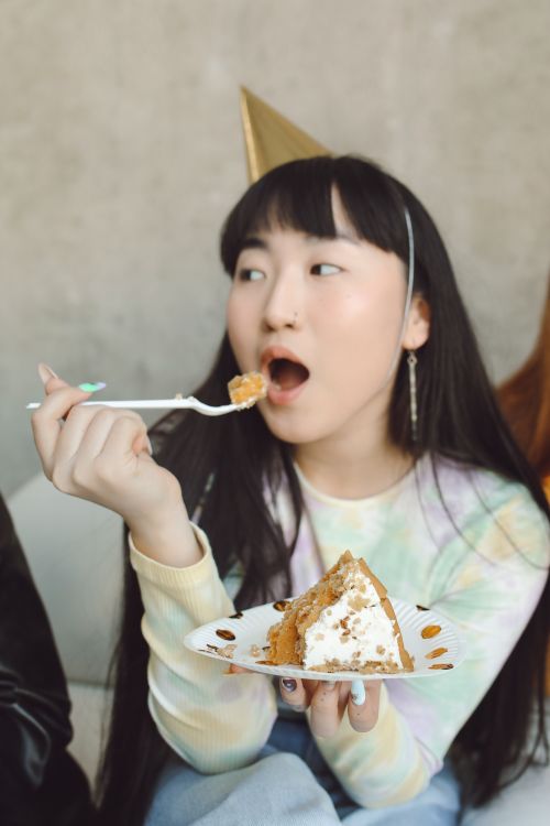 Free Young woman with party hat eating cake at a birthday celebration indoors. Stock Photo