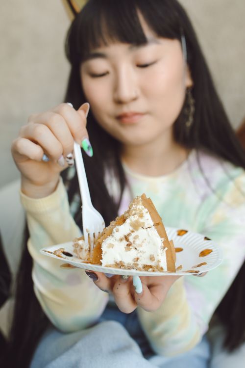 Free Young Asian woman enjoying a piece of cake during a birthday celebration indoors. Stock Photo