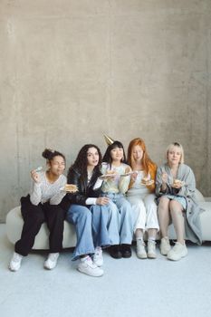 Five diverse women enjoying a birthday celebration indoors with cake and smiles.