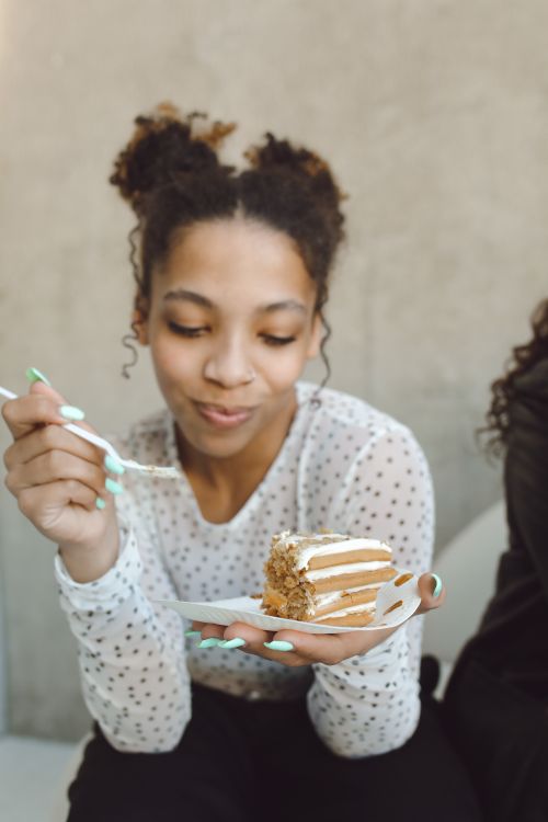 Free A cheerful young woman enjoys a slice of cake indoors, savoring a delightful moment. Stock Photo