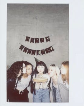 Group of diverse teenagers celebrating a birthday by blowing out candles indoors.