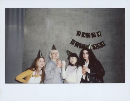 Four friends celebrate a birthday with party hats and drinks, captured in an instant photo.