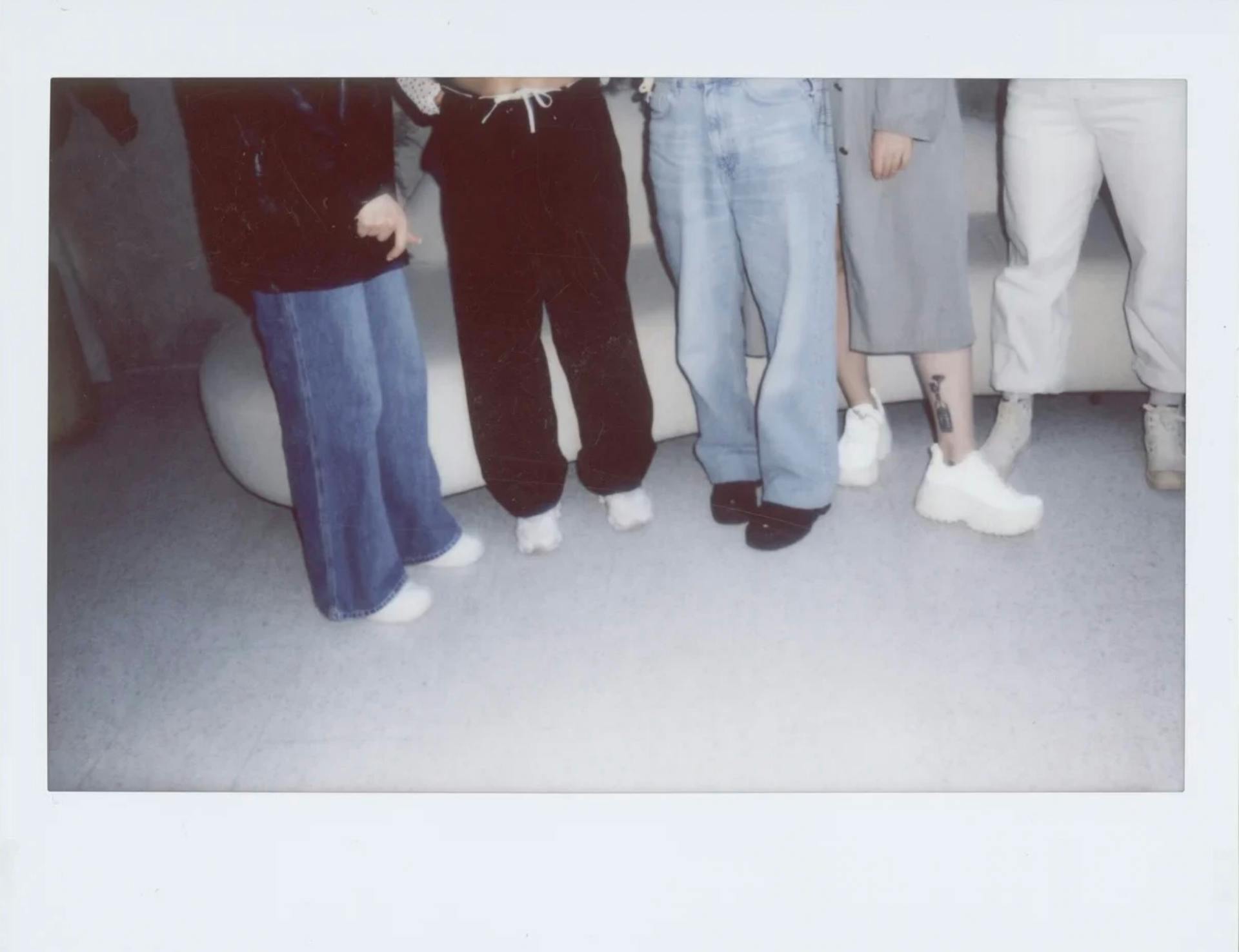 Group of people in casual fashion attire standing indoors, highlighting trendy footwear and denim jeans.