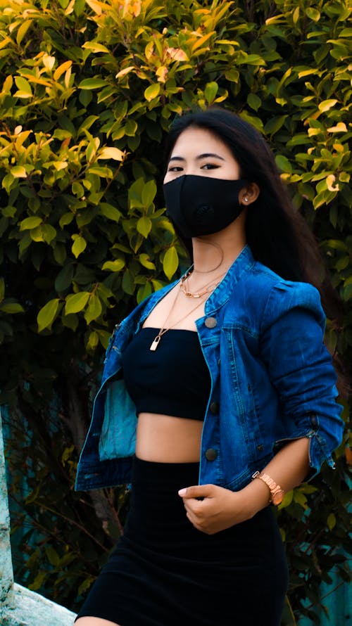 Woman in Blue Denim Jacket and Black Tube Top Wearing Black Face Mask