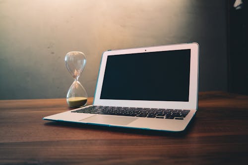 Computer Laptop Beside Hour Glass on Brown Wooden Surface