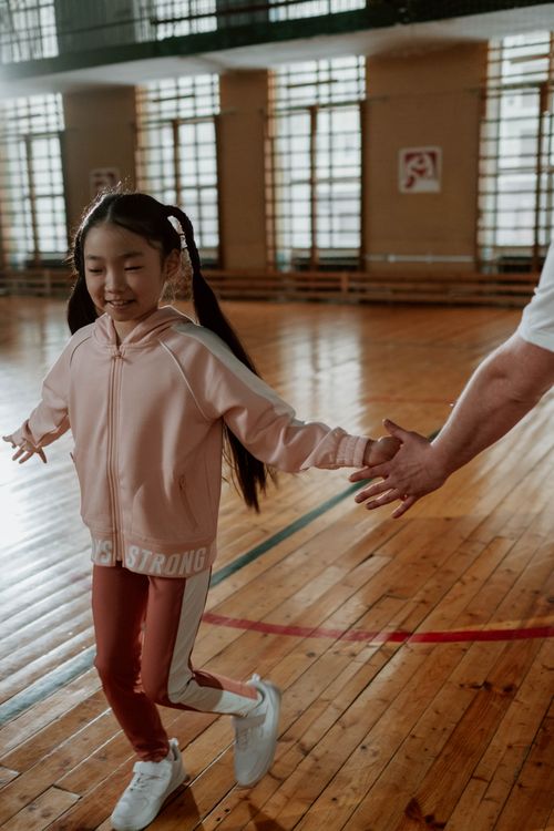 Free A young girl in sportswear practices exercises in a sunlit gymnasium with wooden floors. Stock Photo