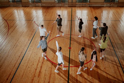 Aerial shot of a dance group rehearsing indoors on a wooden gym floor.