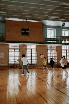 A group of children running in a gymnasium with wooden floors, focusing on motion and exercise.