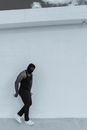 Man in Gray Tank Top and Black Pants Leaning on White Wall