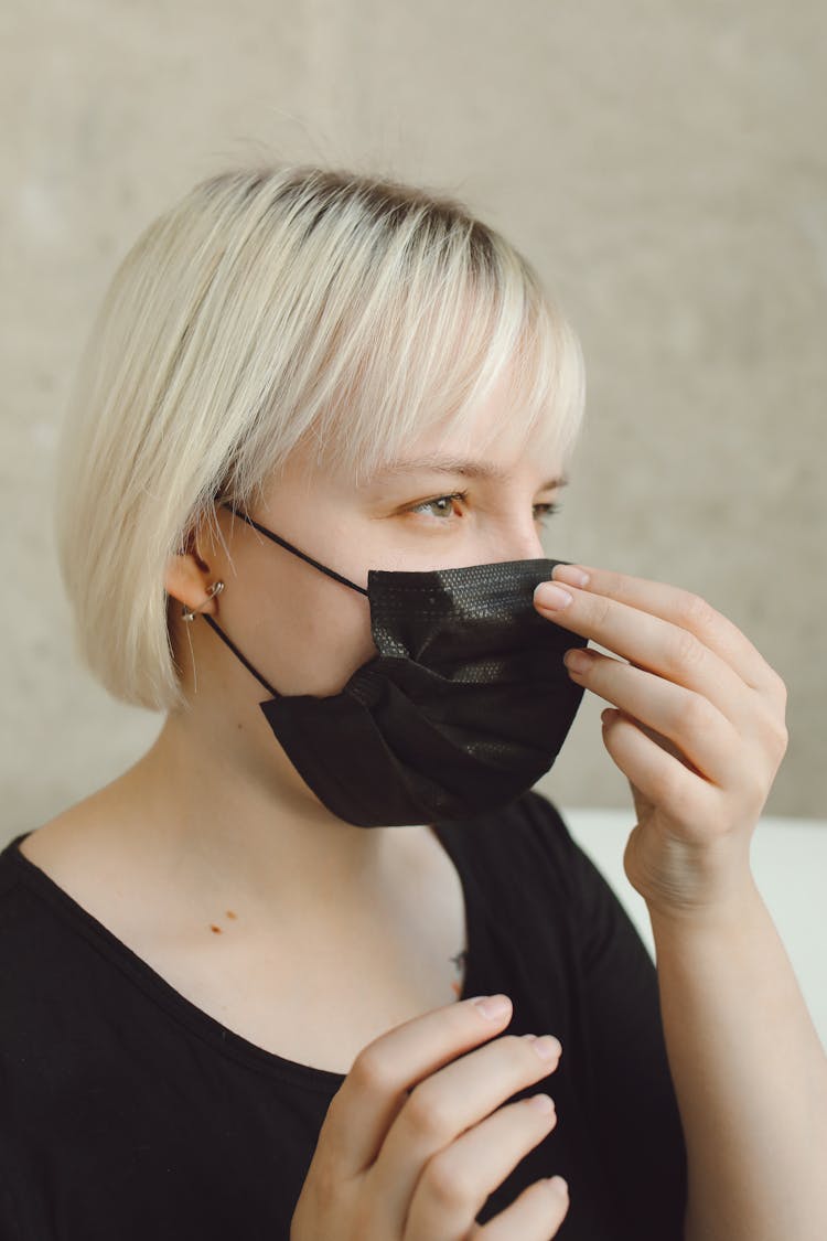 A Woman Wearing A Black Face Mask Touching Her Nose