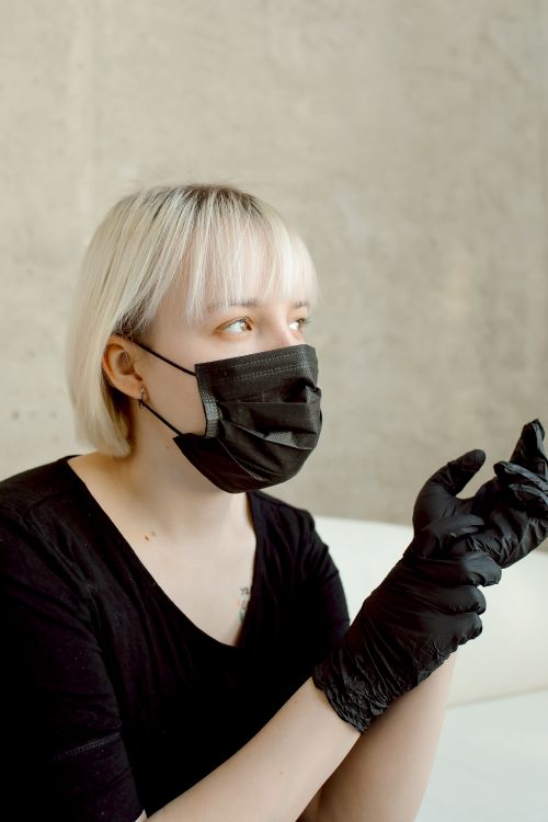 Free Caucasian woman in a black face mask and gloves against a concrete wall. Stock Photo