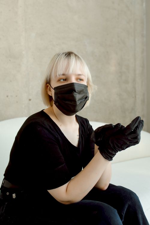 Free Caucasian woman wearing a black face mask and gloves against a concrete background. Stock Photo