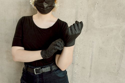 Free A woman in black attire fits gloves against a concrete wall backdrop, emphasizing safety. Stock Photo