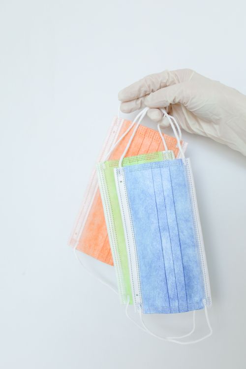 Free A hand in a latex glove holding colorful disposable face masks against a white background. Stock Photo