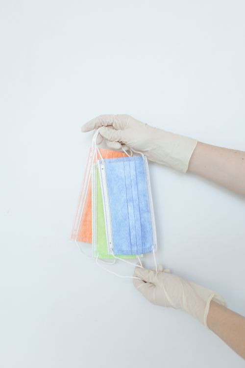 Free Close-up of hands in latex gloves holding colorful disposable face masks against a white background. Stock Photo