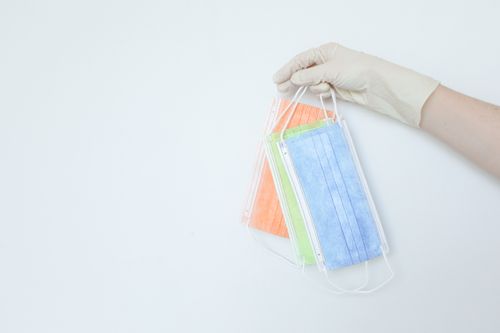 Free A gloved hand holding colorful disposable face masks on a light background. Stock Photo