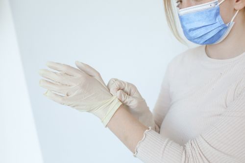 Free Caucasian woman putting on latex gloves with a protective face mask indoors. Stock Photo