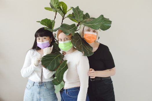 Three Women in Surgical Face Masks Standing Together under Plant Leaves 