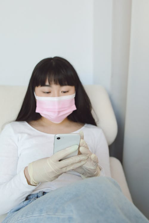 A Woman Wearing a Face Mask and Latex Gloves Using Her Smartphone