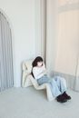 Woman in White Tank Top and Blue Denim Jeans Sitting on White Couch
