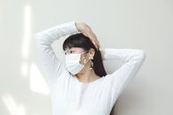 A Woman in White Sweatshirt Wearing Face Mask with Her Hands on Her Head