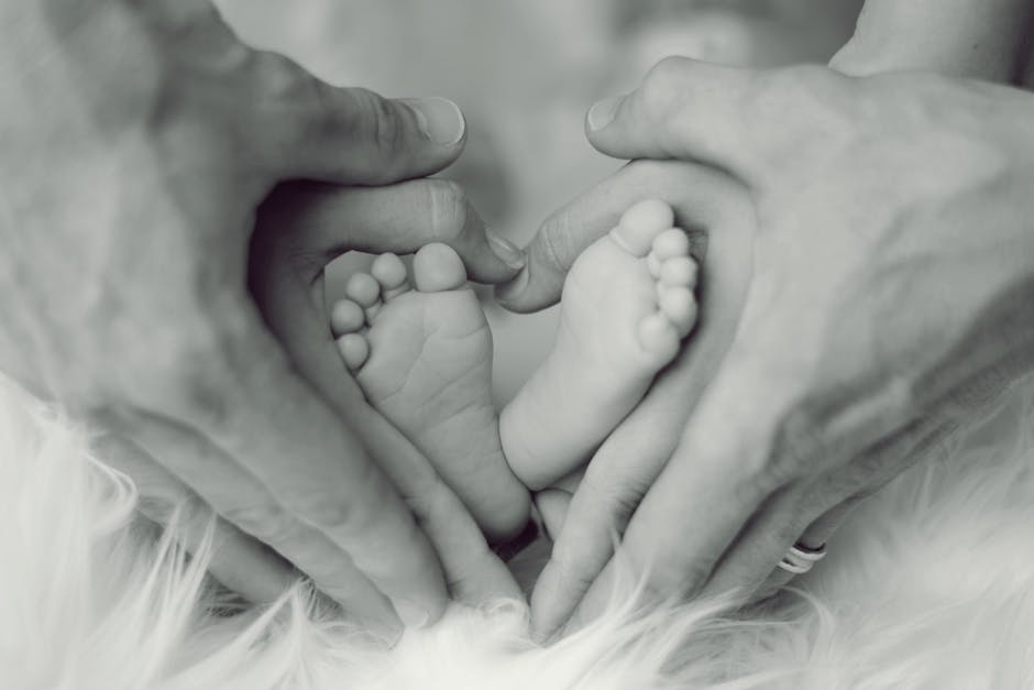 Grayscale Photo of Baby Feet With Father and Mother Hands in Heart Signs