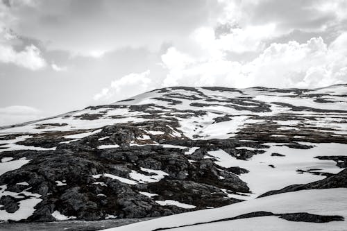 Grayscale Photography of Snow Covered Mountain Under Cloudy Sky