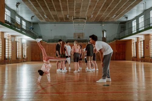 Free Young girl practicing gymnastics in a lively indoor gym environment with a coach. Stock Photo