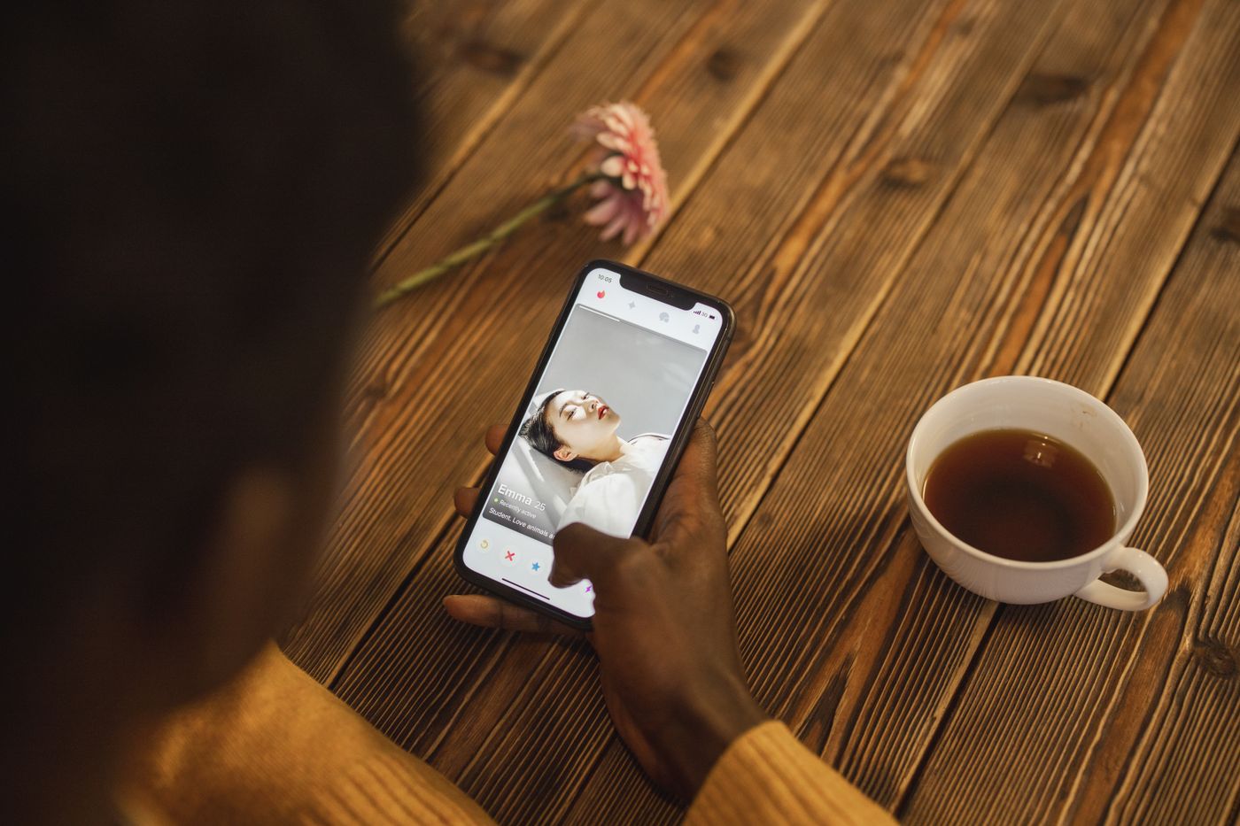 Over-the-shoulder view of a person browsing a dating profile on a smartphone beside a cup of tea