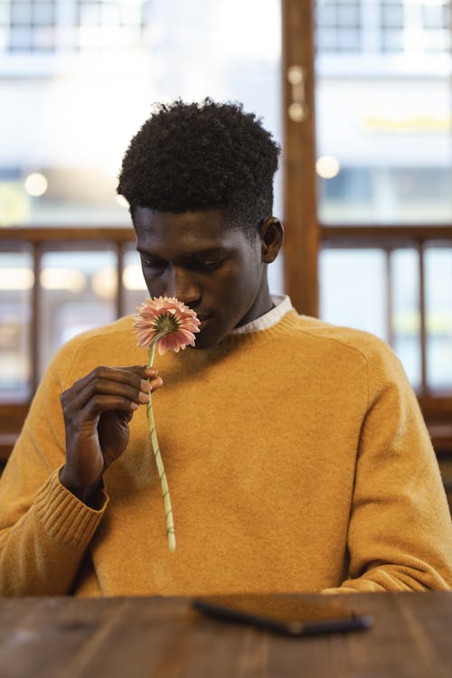 Man Sitting on the Table Smelling a Pink Flower