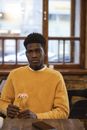 Man in Yellow Sweater Standing Near Brown Wooden Table