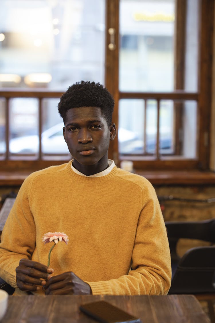 Man Wearing Yellow Sweater While Holding A Flower In The Restaurant