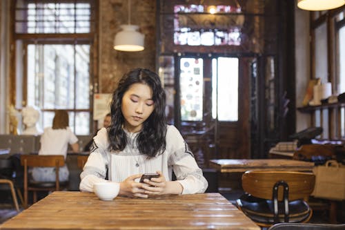 Free Woman Sitting on the Table Holding Her Cellphone Stock Photo