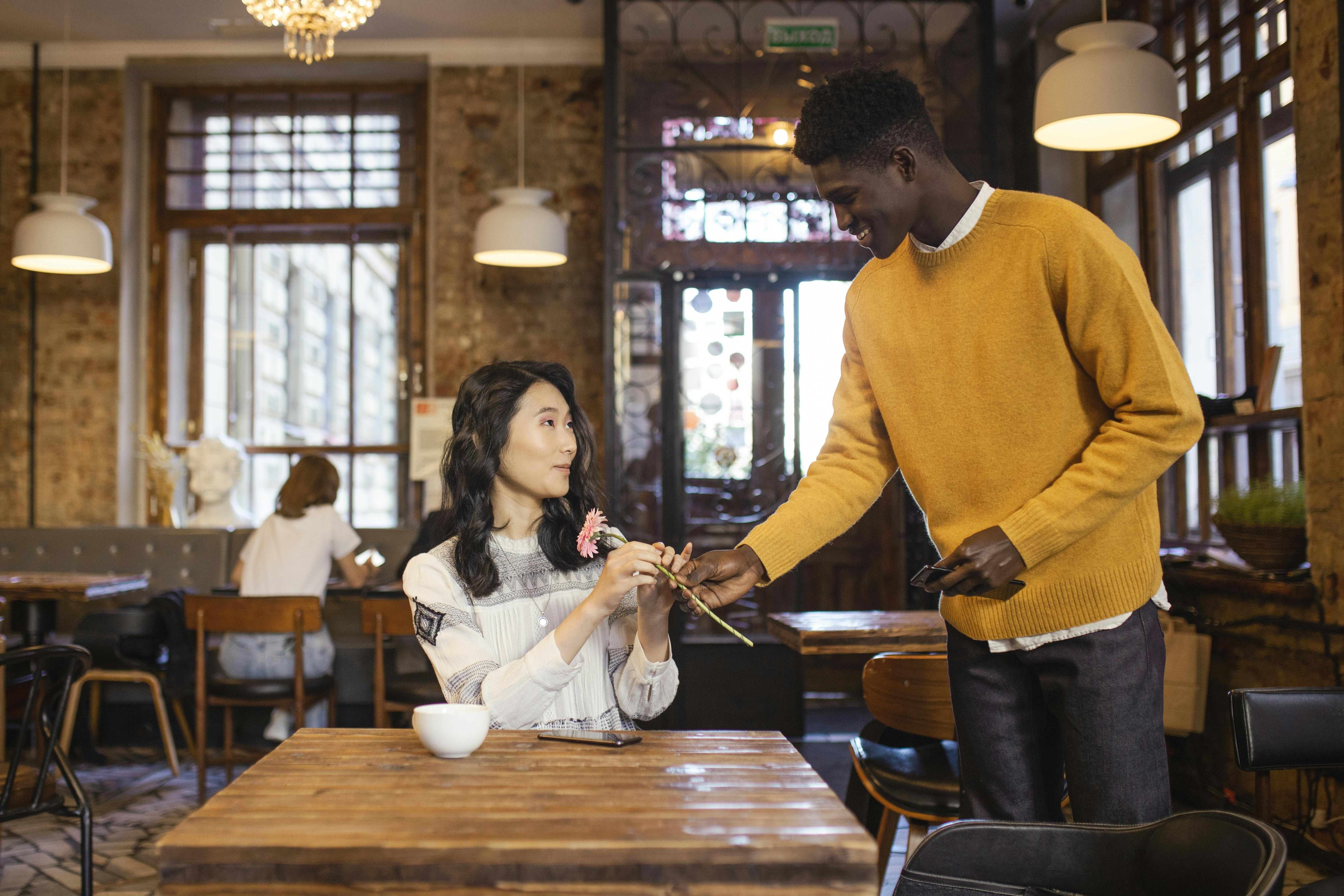 man giving a woman a pink flower on a cafe