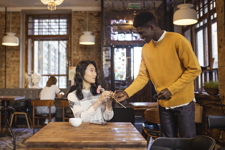 Man Giving A Woman A Pink Flower On A Cafe 