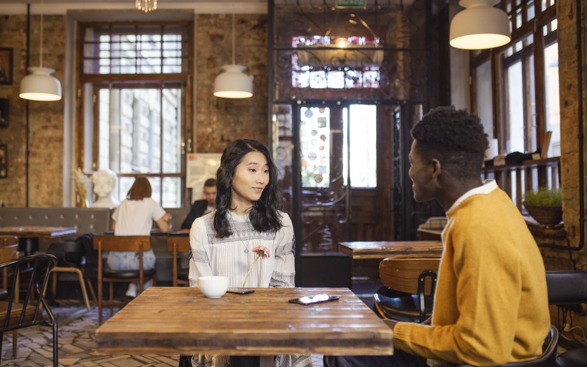Interracial couple sitting in a cozy cafe, engaged in conversation. Interior design includes rustic elements.