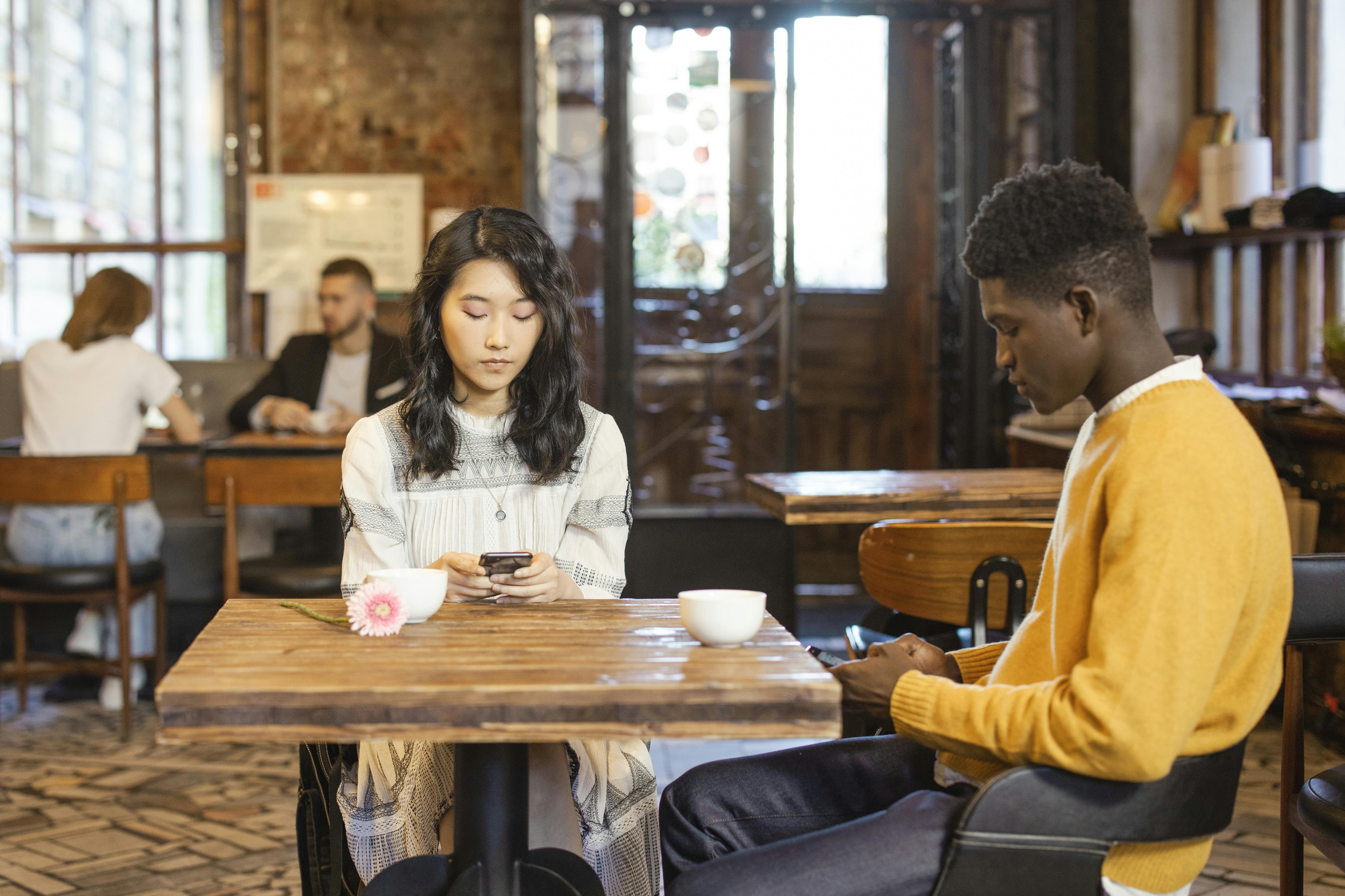 Interracial couple texting while sitting in a modern urban cafe, enjoying a casual meeting.