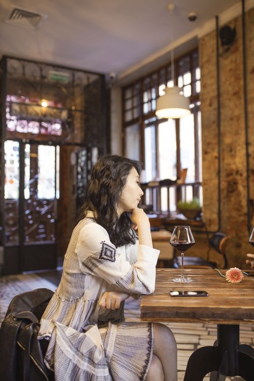 Free Asian woman in a stylish restaurant, sipping wine and using a smartphone, creating a relaxing atmosphere. Stock Photo